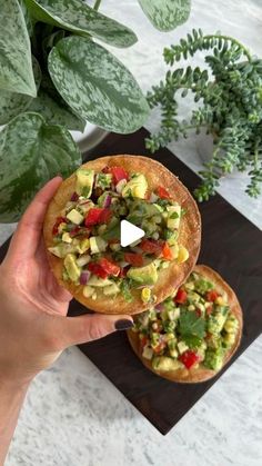 a person holding up a small pizza with toppings on it next to a potted plant