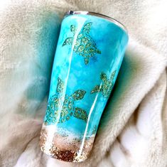 a blue and gold tumbler with sea turtles on it sitting on a white blanket