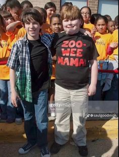 two young boys standing next to each other in front of a group of children wearing yellow shirts