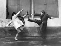 an old photo of two people dancing in the rain with their arms outstretched and legs spread out