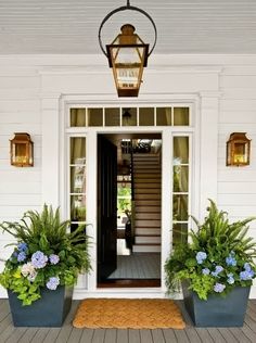 the front entrance to a house with potted plants and a lantern on the porch