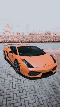 an orange sports car parked in front of a brick wall on the side of a road