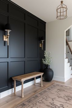 a wooden bench sitting next to a black vase on top of a hard wood floor