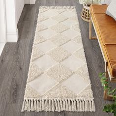 a white rug with tassels is on the floor next to a brown bench