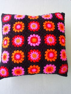 a crocheted pillow is sitting on a white surface with pink, orange and red flowers