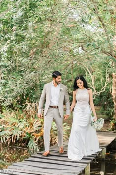 a bride and groom walking across a wooden bridge