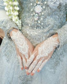 a close up of a person's hands with white lace on them and flowers in the background