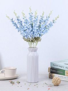 a white vase filled with blue flowers next to two books and a cup on a table