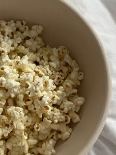 a bowl filled with popcorn sitting on top of a white cloth covered table next to a knife