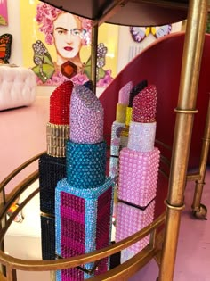 a table topped with lots of different colored bottles on top of a metal stand next to a pink wall