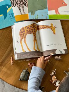 a young boy is reading a book on the table with animals and other things around him