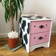 a pink and black painted dresser next to a potted plant