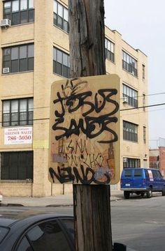 a wooden pole with graffiti written on it in front of a building and cars parked along the street