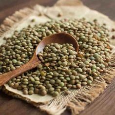 a wooden spoon filled with green lentils on top of a piece of burlied cloth