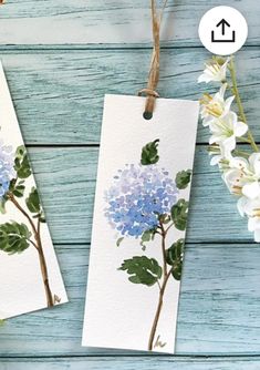 two tags with blue flowers on them are hanging from twine strings next to some white flowers