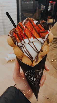 a person holding up an ice cream sundae with chocolate drizzle and strawberries