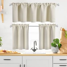 a kitchen with white cabinets and curtains in the window sill, along with potted plants