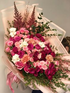 a bouquet of pink and white flowers with greenery in the middle is being held by a woman