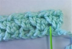 the crochet pattern is being worked on with a green knitting needle in front of it