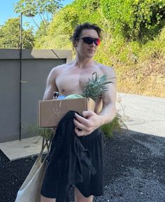 a man with no shirt holding a box and pineapple in his hand while wearing sunglasses