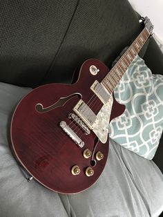 a red electric guitar sitting on top of a couch next to a blue and white pillow