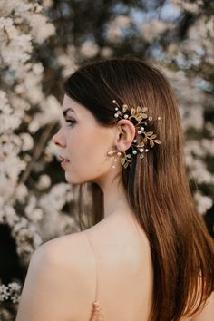 a woman with long brown hair wearing a gold and white flowered headpiece in front of flowers