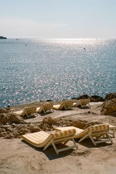 two lounge chairs sitting on top of a sandy beach