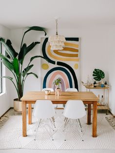 a dining room table with white chairs and a painting on the wall