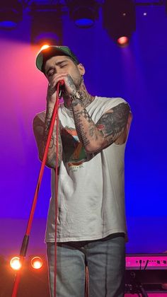 a man with tattoos on his arm holding a microphone in front of purple and blue lights