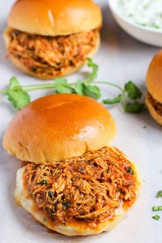 three pulled pork sliders on buns with sauce and parsley sprigs