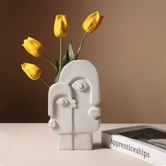 a vase with yellow tulips in it next to a book on a table