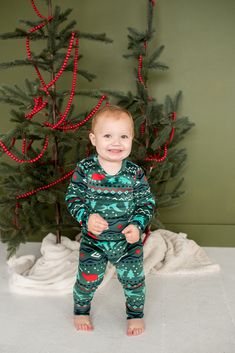 a baby standing in front of a christmas tree