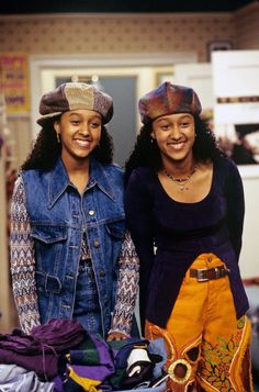 two women standing next to each other in front of clothes and bags on the floor