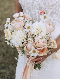 a bride holding a bouquet of white and peach flowers in her wedding dress with an orange sash