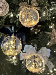 three glass ornaments hanging from a christmas tree with lights on them and bows in the middle