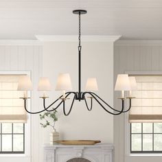 a chandelier hanging over a fireplace in a living room with white walls and windows