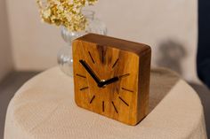 a wooden clock sitting on top of a table next to a vase filled with flowers