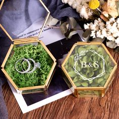 two wedding rings are in glass boxes with moss