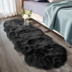 a black sheepskin rug is on the floor in front of a bed and vase with flowers