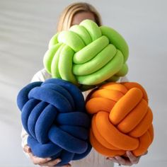 a woman holding four different colored pillows in her hands