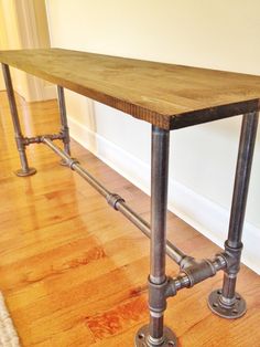 a wooden table sitting on top of a hard wood floor next to metal pipes and piping