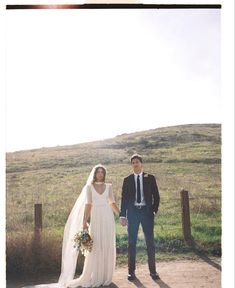 a bride and groom standing in front of a fence on their wedding day at the ranch