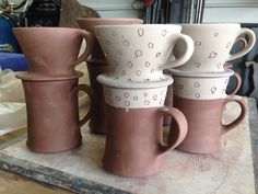 four coffee mugs sitting on top of a wooden table in front of a pile of other cups