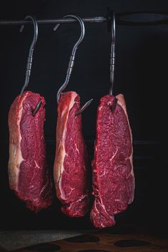 three pieces of raw meat hanging from hooks