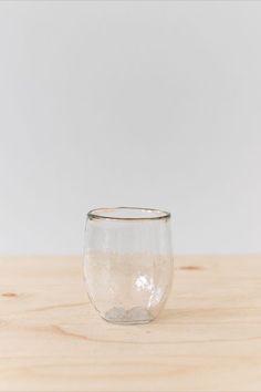 a glass filled with water sitting on top of a wooden table next to a white wall