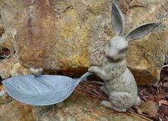 a statue of a rabbit with a leaf in its mouth sitting on the ground next to a rock