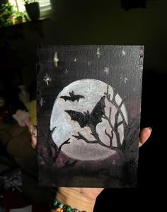 a person holding up a piece of art that looks like a bat on a full moon