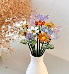 a white vase filled with colorful flowers on top of a table next to a dried plant