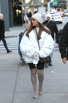 a woman walking down the street wearing boots and a white jacket with fur on it