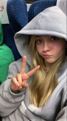 a girl in a gray hoodie making the peace sign